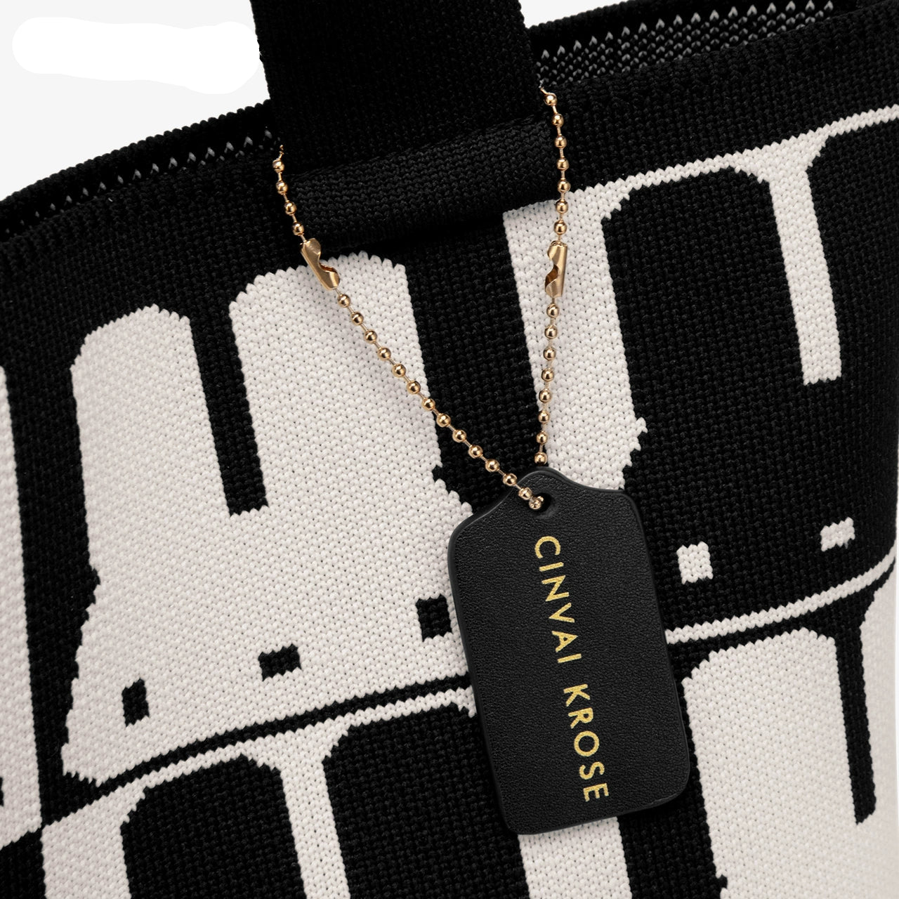 Black dog tag with 'CINVAI KROSE' text on a black and white patterned background